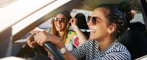 Laughing trendy young college graduates in sunglasses traveling in a car in town, happy because they just bought their first car after graduation