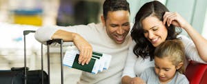 Young family gathered around a sheet learning about what they need to know about using debit cards internationally, waiting at an airport holding luggage, tickets, and passports. Young family gathered around a sheet learning about what they need to know about using debit cards internationally, waiting at an airport holding luggage, tickets, and passports.