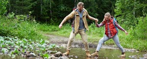 A father and daughter cross a creek as he gives her a clear and simple credit card definition while learning about financial literacy.