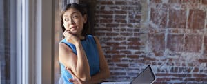 Woman looking out a window while leaning against a brick wall