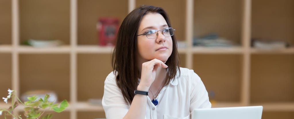 Young woman sitting in front of a laptop and looking thoughtful