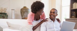 Young couple in their living room, learning about a cash out refinance on their laptop.