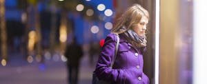 Young woman looking at store window in the city at night, trying to relieve her stress with shopping.