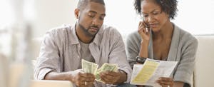 Young couple looking at their bills and struggling financially, wondering who to ask for help.