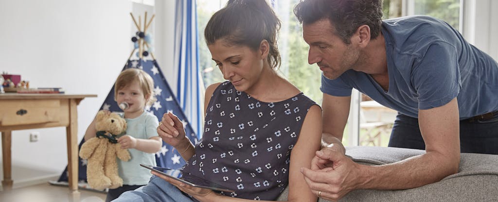 Couple using tablet at home with toddler son in background