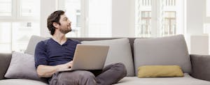 Man sitting on couch using laptop, looking hopeful