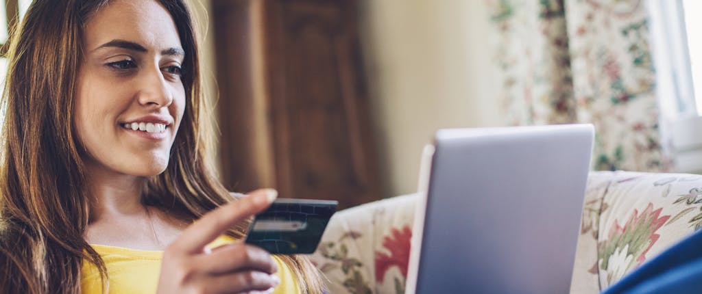 Woman wondering what is a balance transfer fee while she is lying down on a couch with her laptop and credit card.