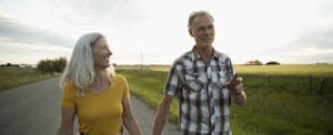 Couple farmers holding hands, walking on road along farm
