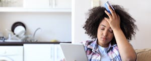 Stressed woman holding credit card and tablet, trying to figure out what to do after identity theft