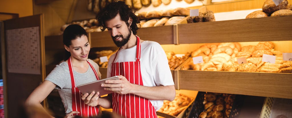 Couple using digital tablet in bakery shop.