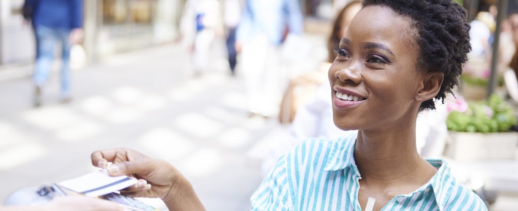 A woman smiles while handing her credit card to server at an outdoor cafe.
