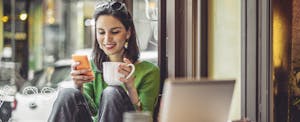 Young woman in a coffee shop drinking coffee and looking at her cell phone