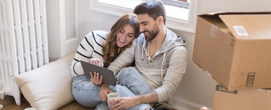 Young couple sitting in room full of boxes, looking at digital tablet