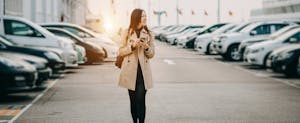 Young woman holding cell phone and walking in parking lot