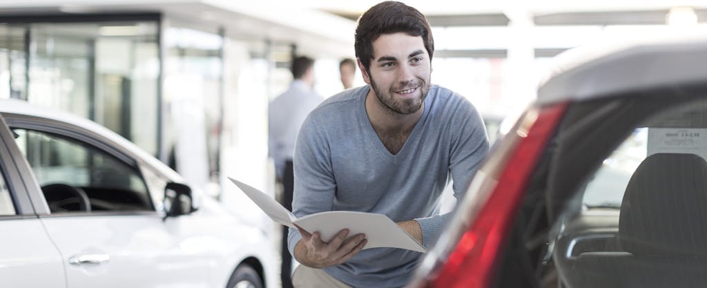 Smiling man looking at new car at car dealership