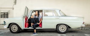 how-to-get-classic-car-loan Woman sitting in her vintage car with the door open, as she looks into the distance