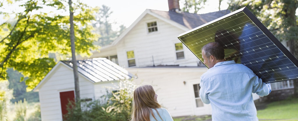 Man carrying a solar panel and talking to his young daughter