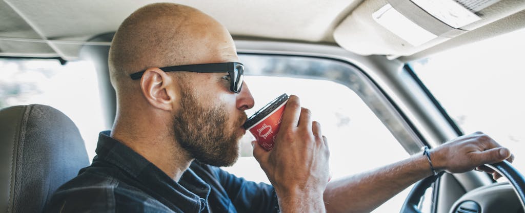 Man driving a car, sipping from a cup of coffee
