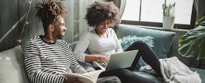 Young couple sitting on couch, reading book and using laptop