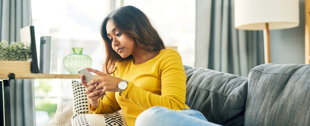 Young woman using her cellphone while relaxing at home on the couch