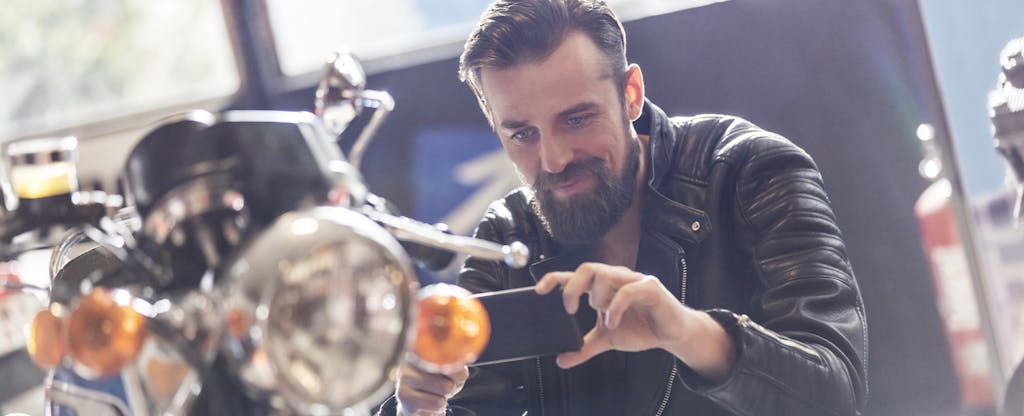 Man with camera phone photographing motorcycle in shop