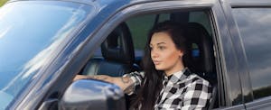 Woman with tattoo sitting behind the wheel of her car and looking at the road