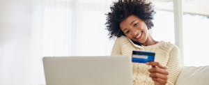 Woman sitting on sofa at home, talking at the phone and looking at her debit card security code