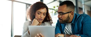 Man and woman sitting together at a table, reading on a tablet about when quarterly taxes are due