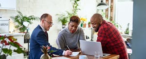 Couple sitting with a financial adviser in their kitchen, reading together about the best options for a personal loan with a co-signer