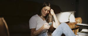 Woman sitting on the floor of her bedroom, reading on her phone about free savings account options