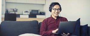Man sitting on his couch, smiling and reading on his laptop about the benefits of a savings account