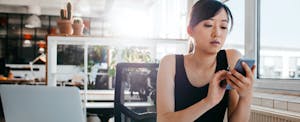 Young woman at work on her phone, looking up why interest rates are so low on savings accounts