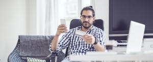 Young man working at home and holding up a credit card