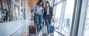 united-gateway-card-review_1010633980 Two women with suitcases walking through airport and talking