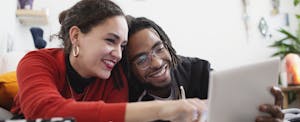 Man and woman, smiling and sitting together as they read about NOW accounts on a tablet