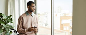 Man reading about having a mixed credit file on his phone and looking thoughtfully out the window