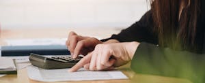 Closeup of woman's hands as she makes calculations while looking through bills
