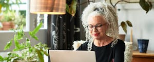 A woman seated at a table smiles as she uses her laptop to book a vacation using a book now pay later service.