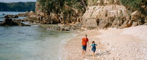fly-now-pay-later A father and small child walk along a beach in the sunshine.
