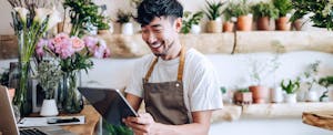 A florist surrounded by plants smiles as he uses a tablet to research loans like Lendly.