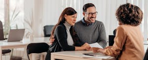 promissory-notes A couple sit at a table opposite their loan rep as they review a promissory note together.
