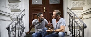 Two men sitting together outside on their stoop, discussing the average home value increase per year