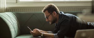 Man lying on his couch, reading on his phone about the best auto insurance for high-risk drivers