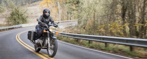 best-motorcycle-insurance A woman wearing a helmet and protective clothing rides a motorcycle down an empty road in winter.