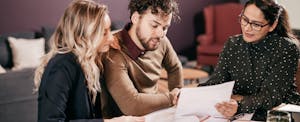 A couple seated at a table review the details of their mortgage refinance with their loan representative.