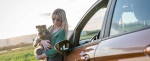 Woman on a road trip, smiling as she holds her dog while on the side of the road