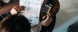 Overhead view of young Asian woman managing personal banking and finance at home. Planning budget and calculating expenses while checking her bills with calculator. Managing taxes and financial bills.