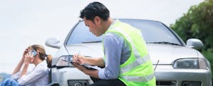 best-insurers-bad-credit Male insurance claim adjuster examining vehicle damage while woman is sitting next to the car talking on her phone.